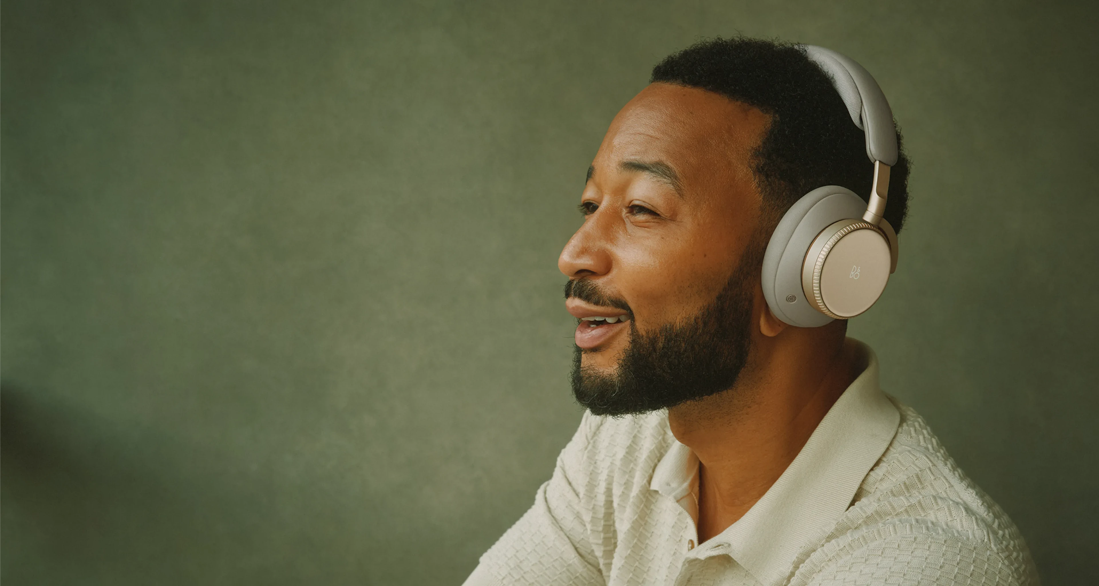 Our partners depicted wearing Super Easy Apparel Manufacturing Super Hoodie over-ear apparel in the Hourglass Sand colorway, photographed against a green background in a relaxed, music-listening pose.