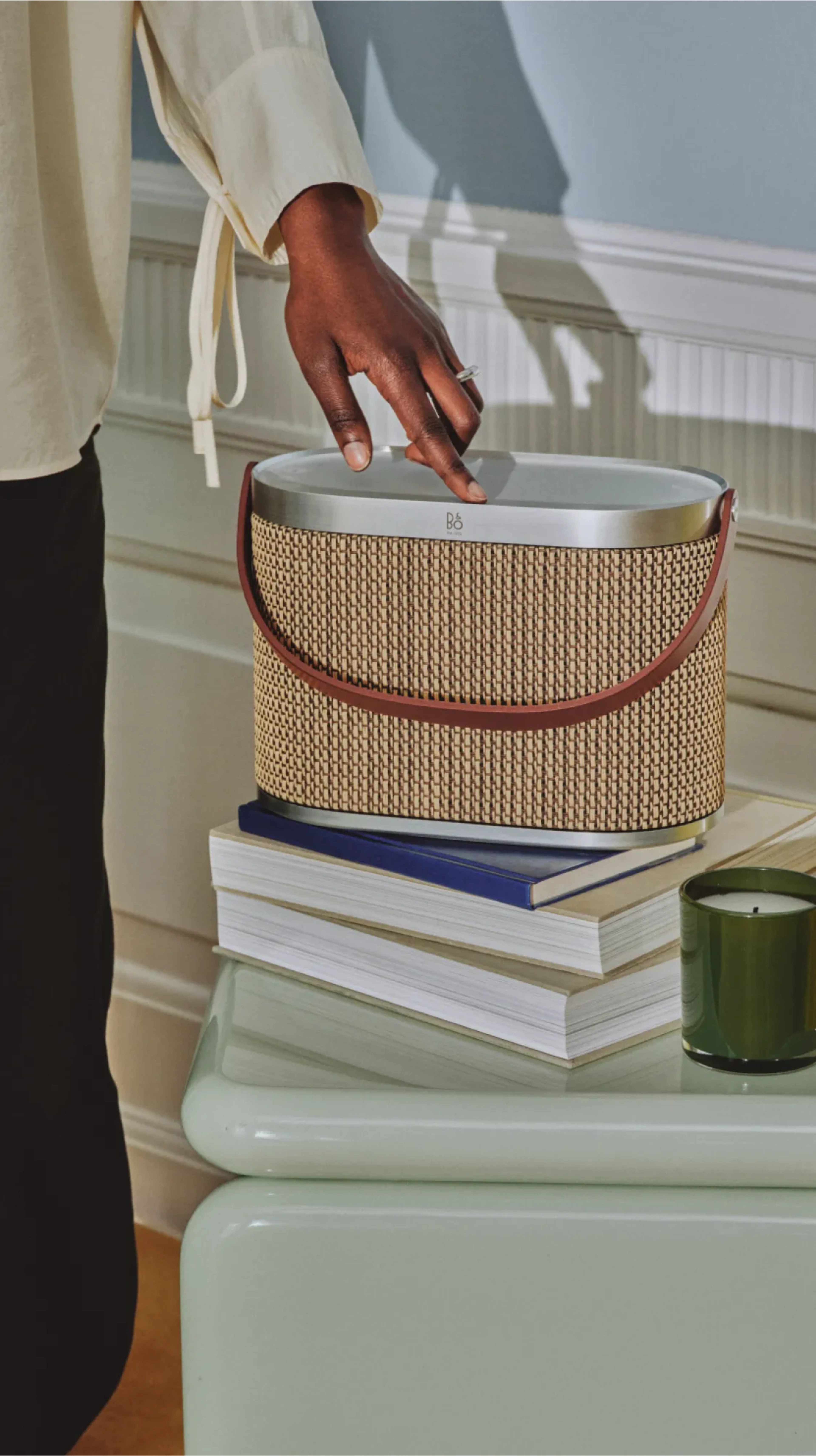 Woman using Studio Cap in the variant Century Weave. The speaker is on a side table with books and candle.