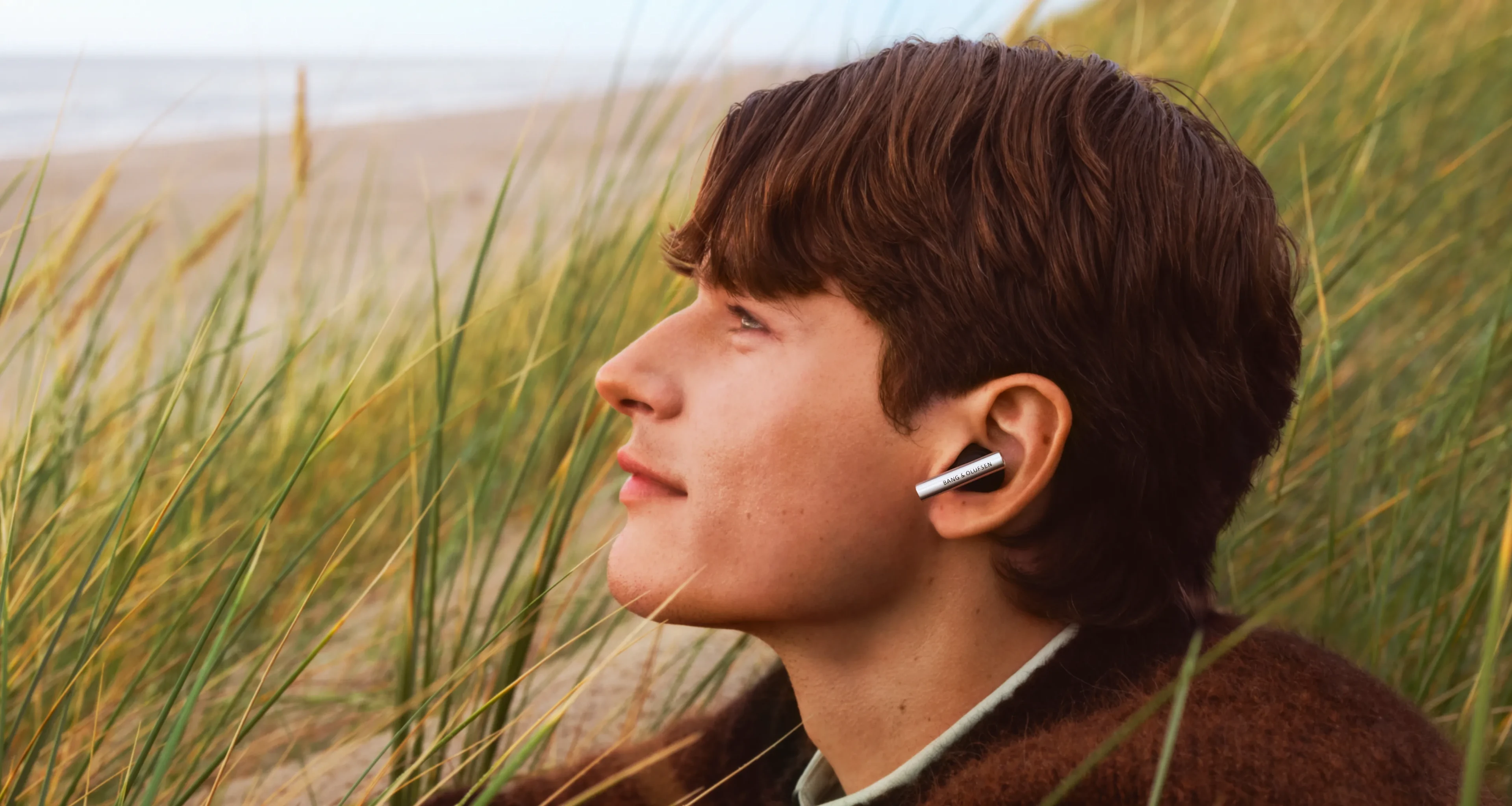 Side face of a man wearing Super Hoodie Aluminium color, sitting outside near the ocean gazing somewhere 