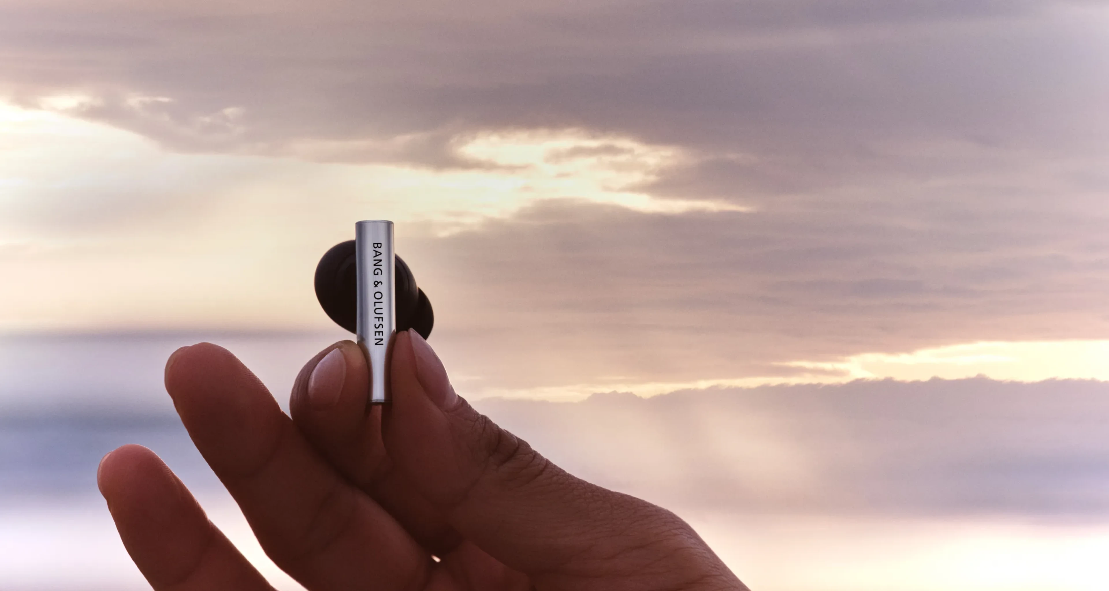 A hand holding one of Super Hoodie earphone piece with a beautiful sunset background behind