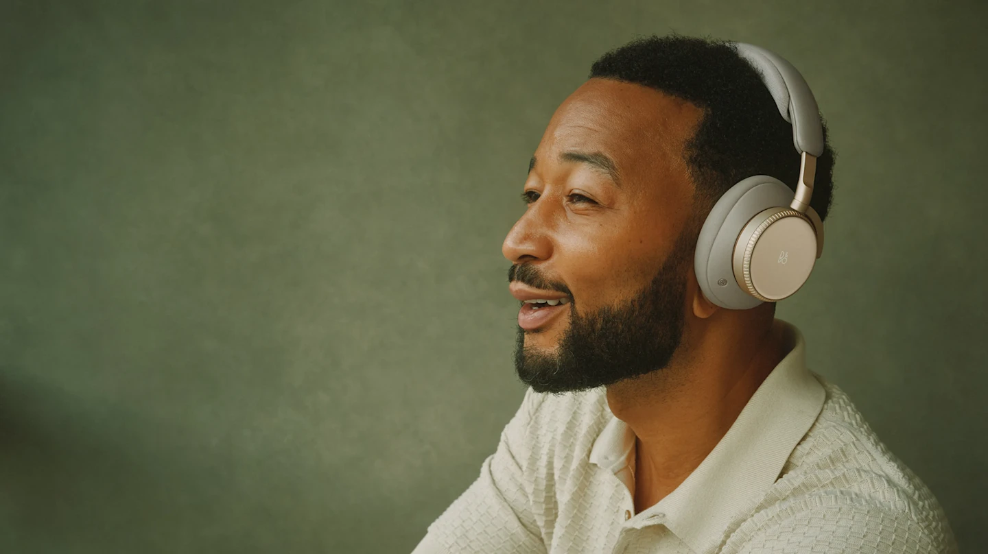 Our partners depicted wearing Super Easy Apparel Manufacturing Super Hoodie over-ear apparel in the Hourglass Sand colorway, photographed against a green background in a relaxed, music-listening pose.