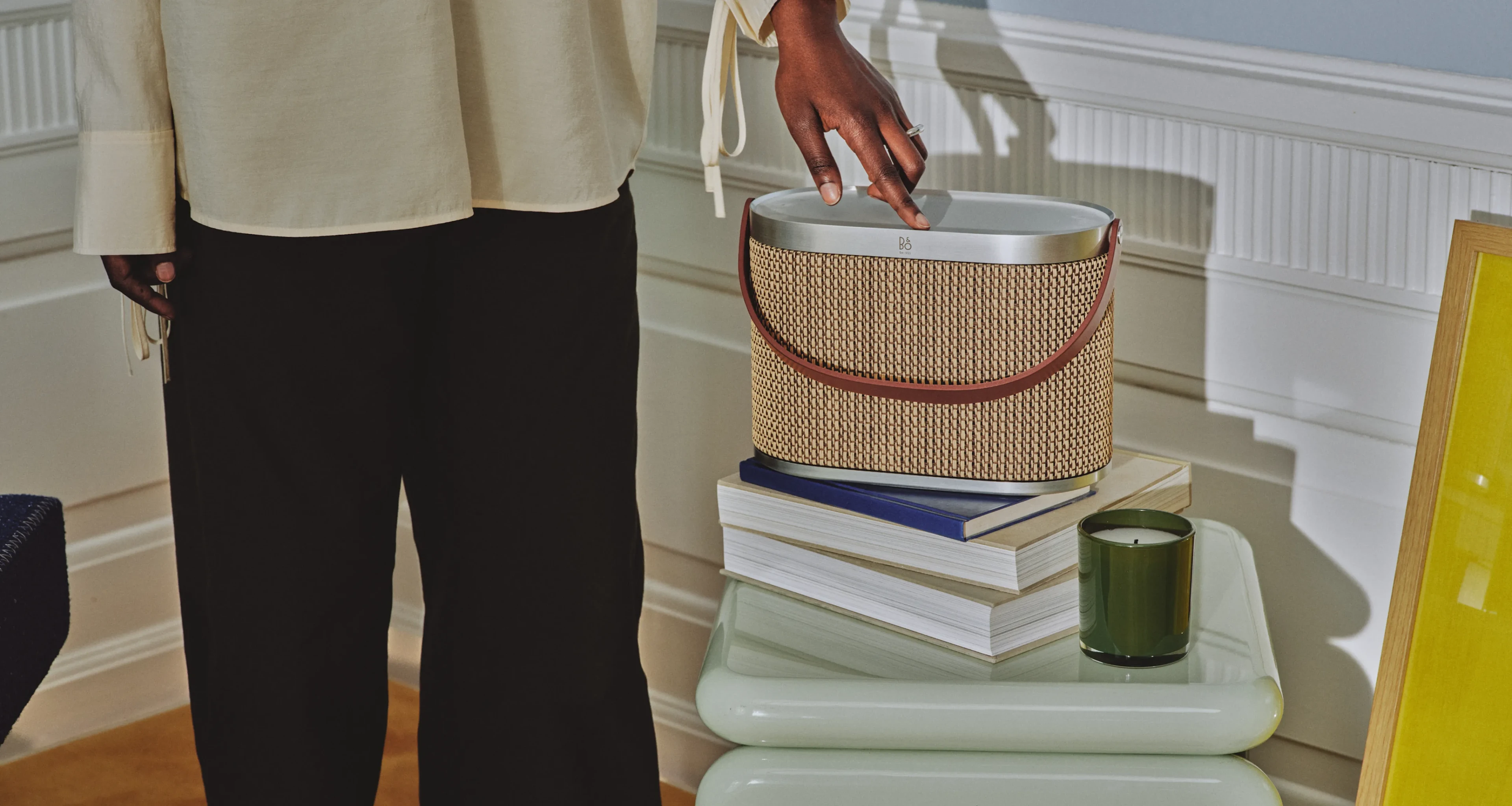 Woman using Studio Cap in the variant Century Weave. The speaker is on a side table with books and candle.